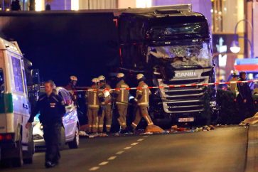 Police and emergency workers stand next to a crashed truck at the site of an accident at a Christmas market on Breitscheidplatz square on Monday, Dec 19