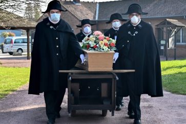 TOPSHOT - Members of the Charitable Brotherhood of Saint-Eloi de Bethune, each wearing a face mask, carry a coffin towards a grave, at Pierrette cemetery in Bethune, on March 27, 2020, as the country is under lockdown to stop the spread of the Covid-19 pandemic caused by the novel coronavirus. - Founded in 1188, the Charitables have for eight centuries taken care of funerals for the inhabitants of Bethune regardless of religion or wealth. Rarely, though, are they done behind almost-closed doors. (Photo by DENIS CHARLET / AFP)