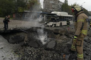 FILE - Firefighters and police officers work at a site where an explosion created a crater on the street after a Russian attack in Dnipro, Ukraine, Monday, Oct. 10, 2022. (AP Photo/Leo Correa, File)